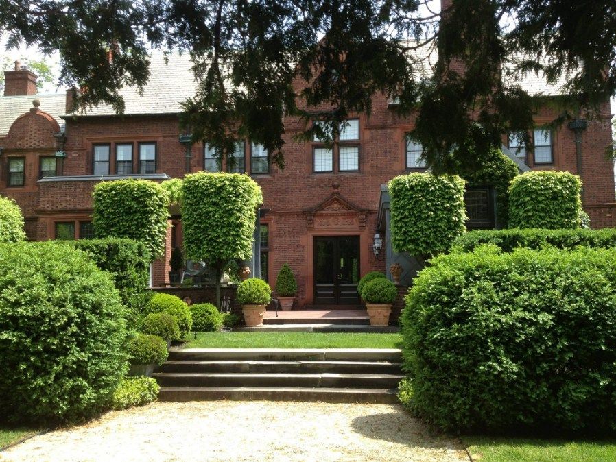 Red brick mansion with manicured bushes and a stone stairway leading to the front door.