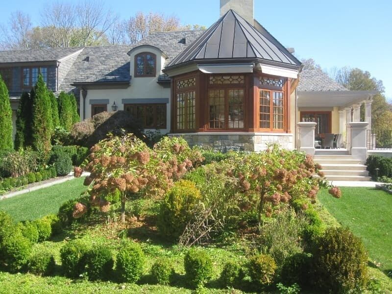 House with a multi-level garden featuring green shrubs and trees.