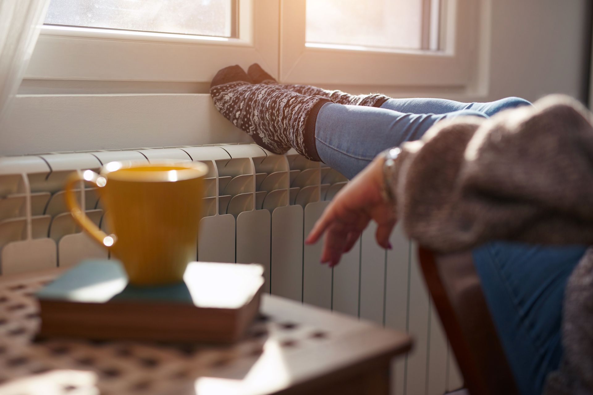 Woman warming feet next to heater after a fall tune-up on a residential heating system in Fort Smith