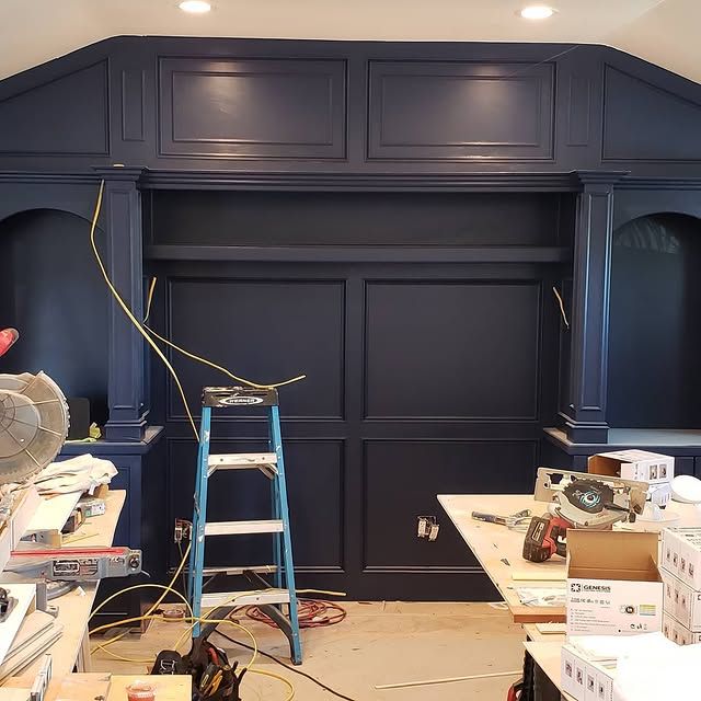 A dark blue custom built-in entertainment center under construction, featuring shelves, panels, and exposed wiring.