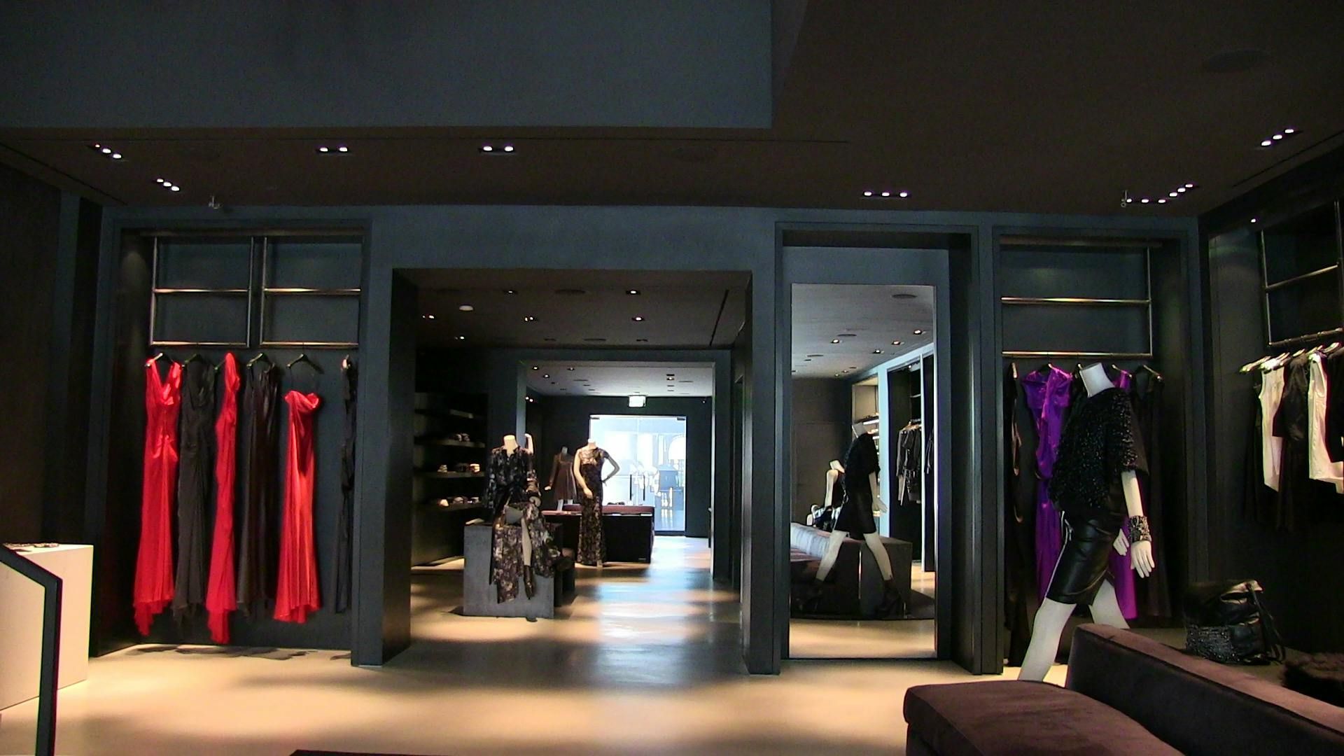 A sleek, dark-themed boutique with clothing racks on both sides, a central archway, and mannequins displaying apparel.