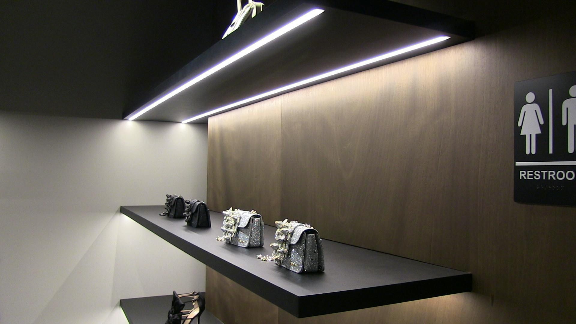 A modern retail display with floating shelves holding handbags, illuminated by LED lights against a wooden wall.