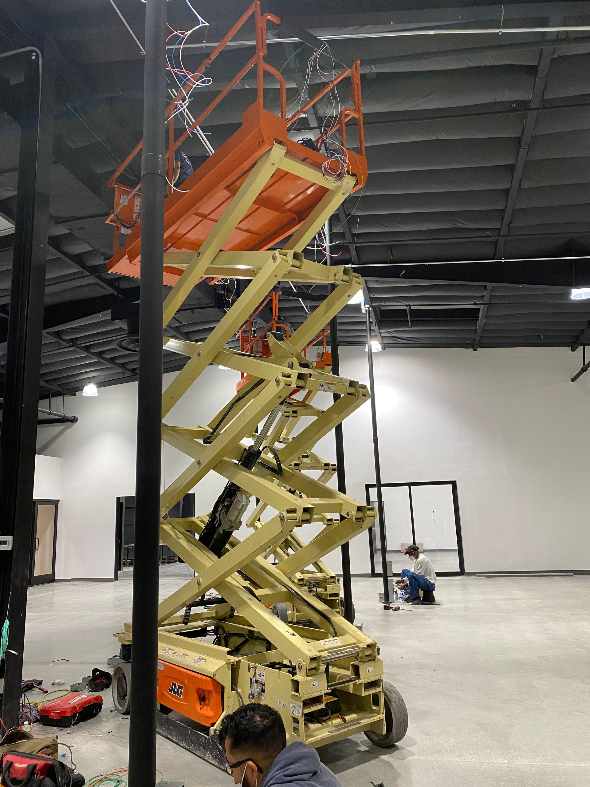 Yellow-orange scissor lift raised inside an industrial warehouse with a worker nearby