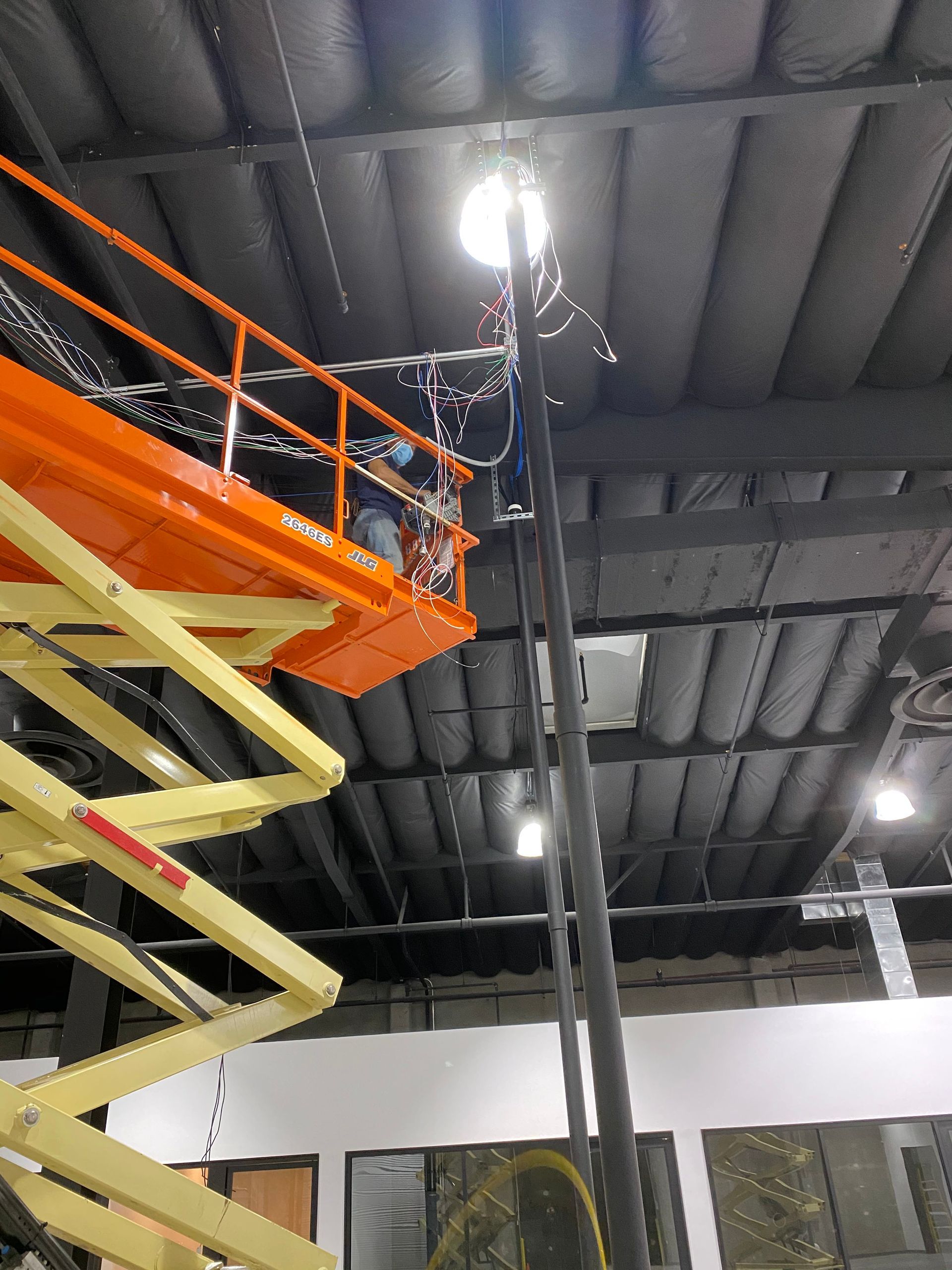 Orange scissor lift extended toward a bright ceiling light in an indoor warehouse or industrial space
