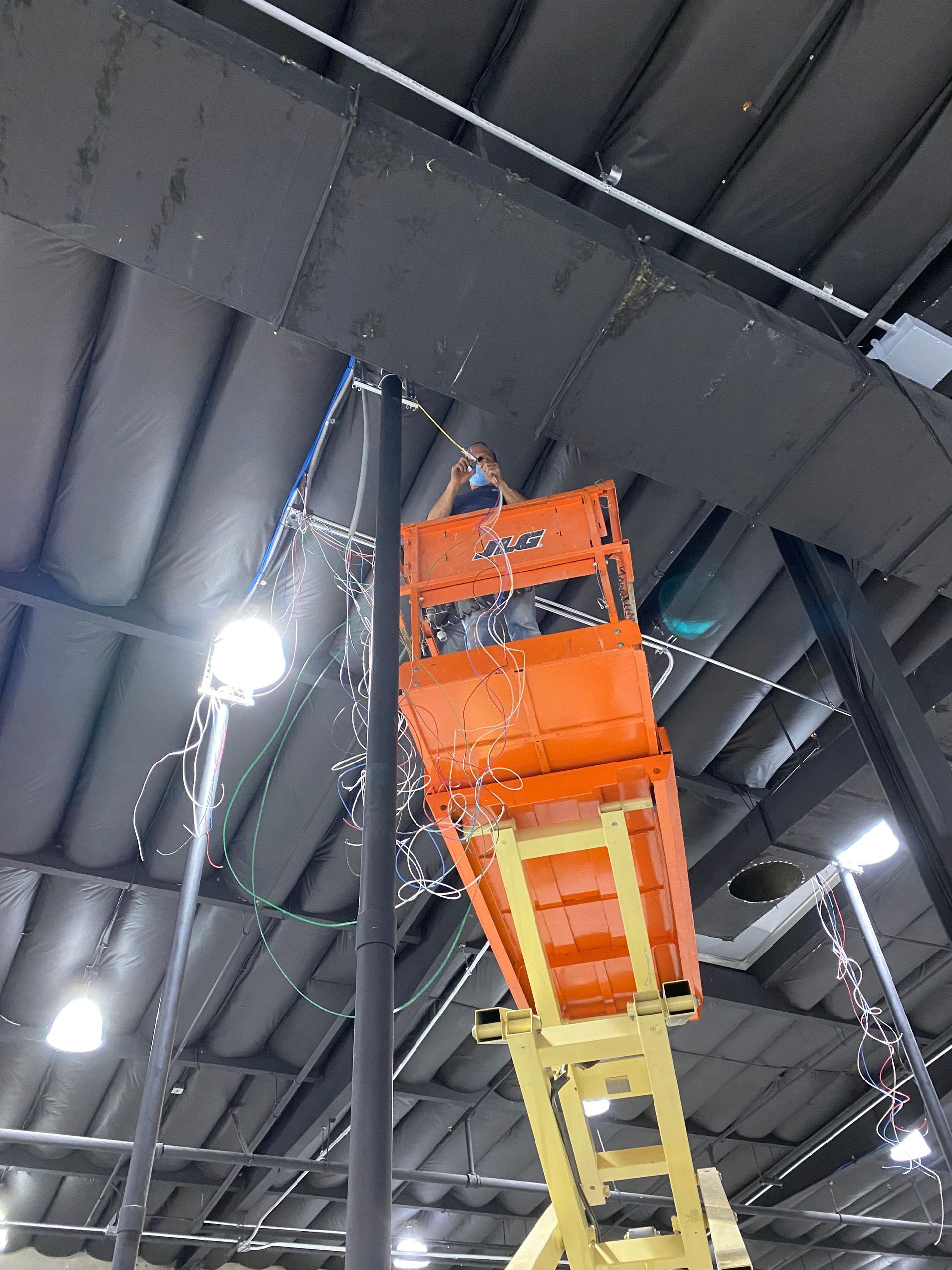 Orange and yellow scissor lift raised inside a warehouse with metal ceiling beams and bright lights
