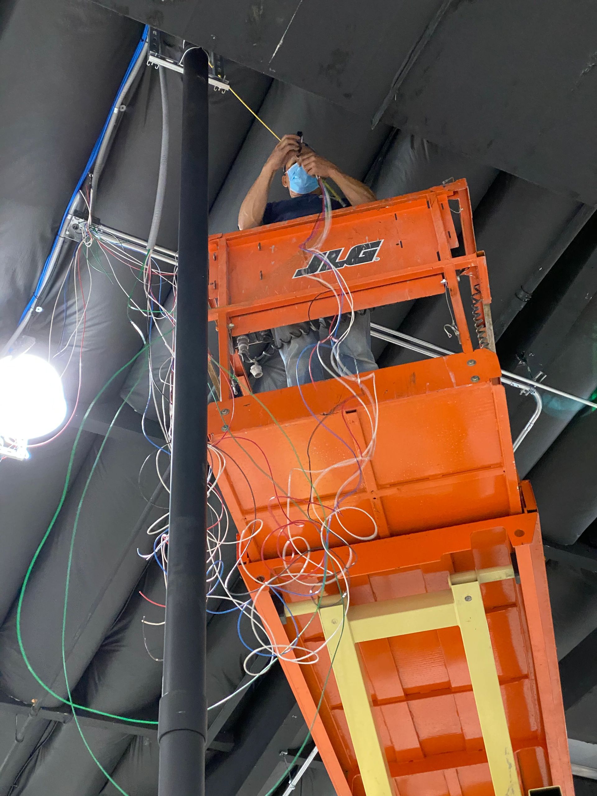 Person on an orange scissor lift working near ceiling lights and exposed cables