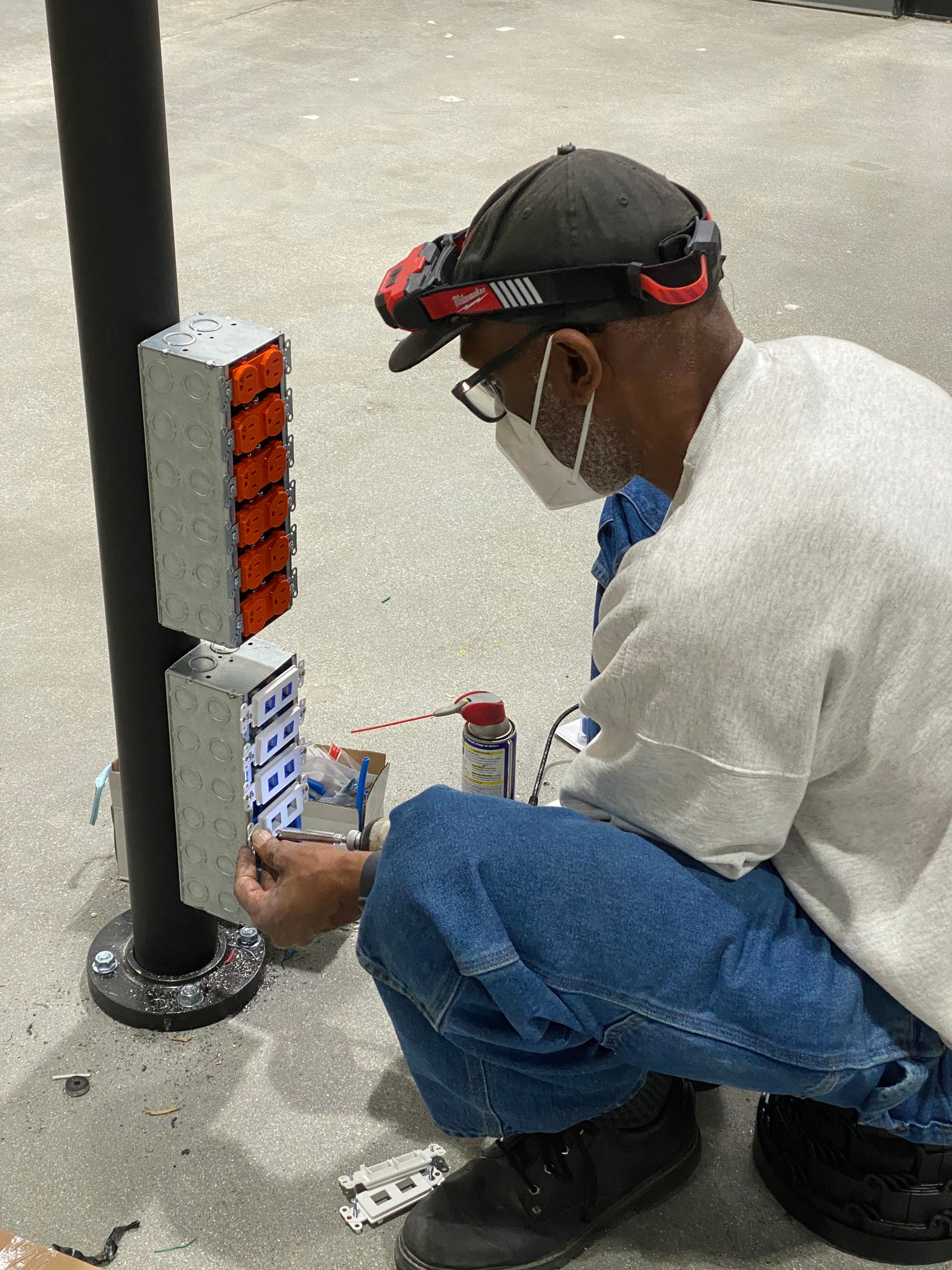 Worker crouching beside a pole, adjusting a mounted orange-and-white device indoors.