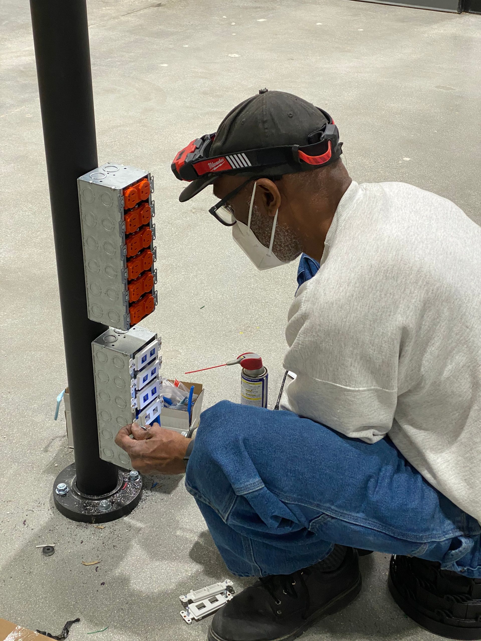 Person crouching by a black post, inspecting orange and white labels on a concrete floor.