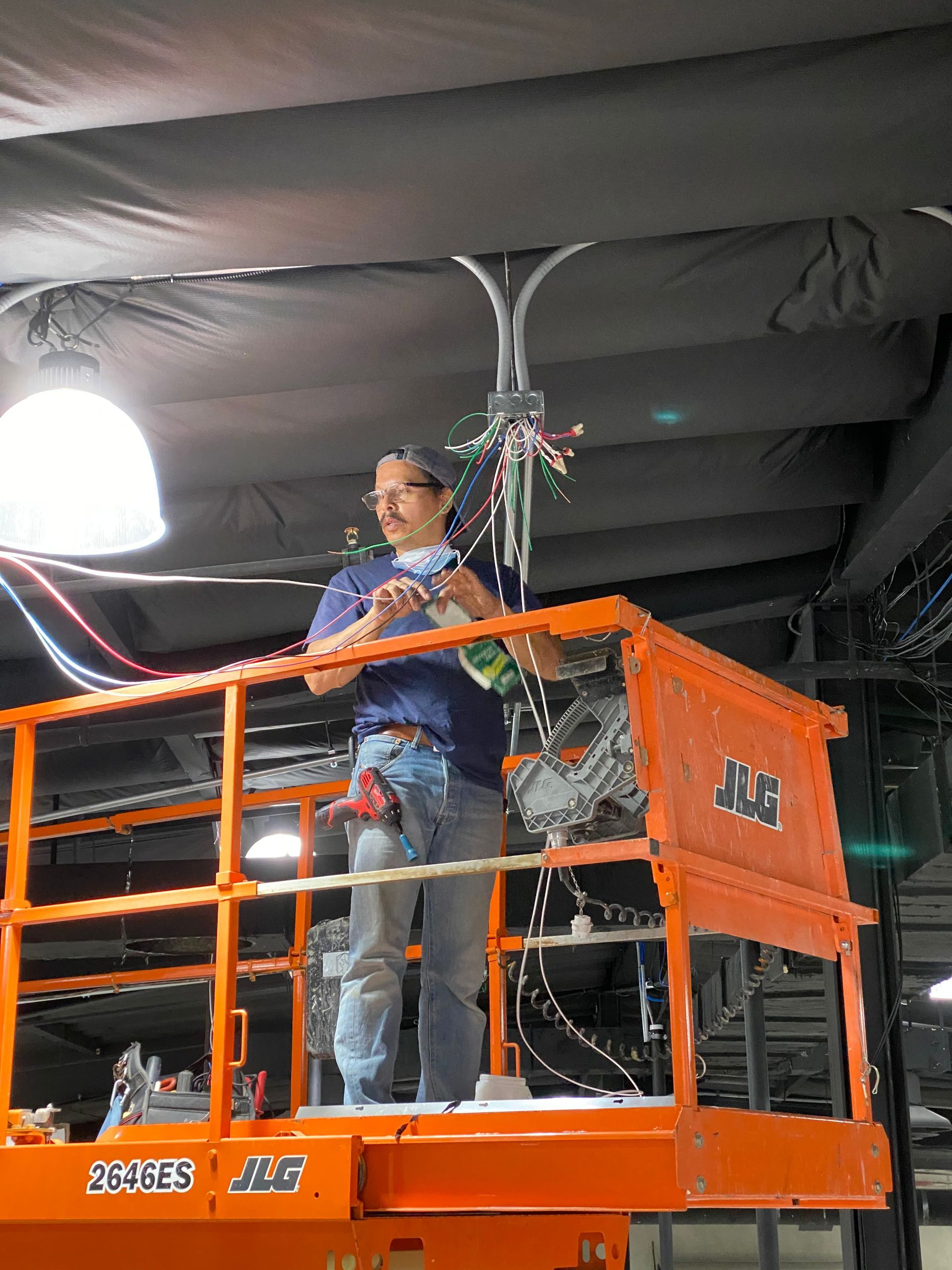 Worker standing on an orange lift inside a dark indoor venue, adjusting decorations overhead