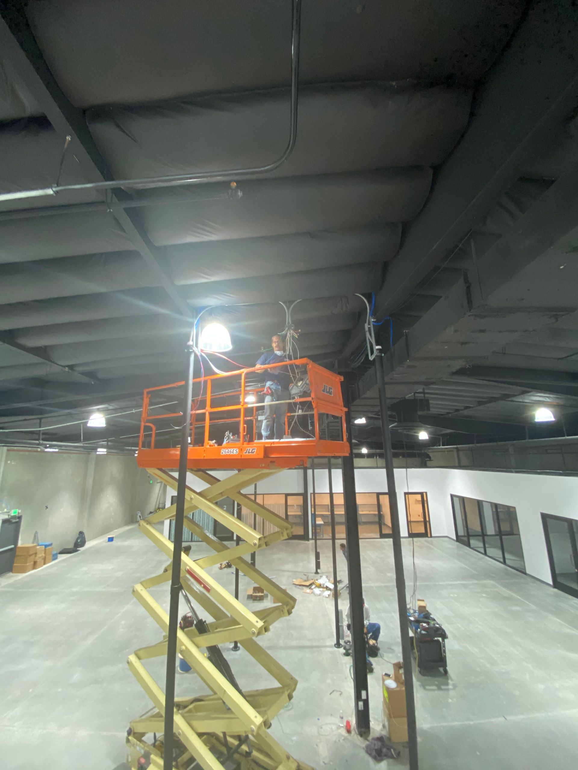 Orange scissor lift and workers under a high industrial ceiling in a warehouse interior
