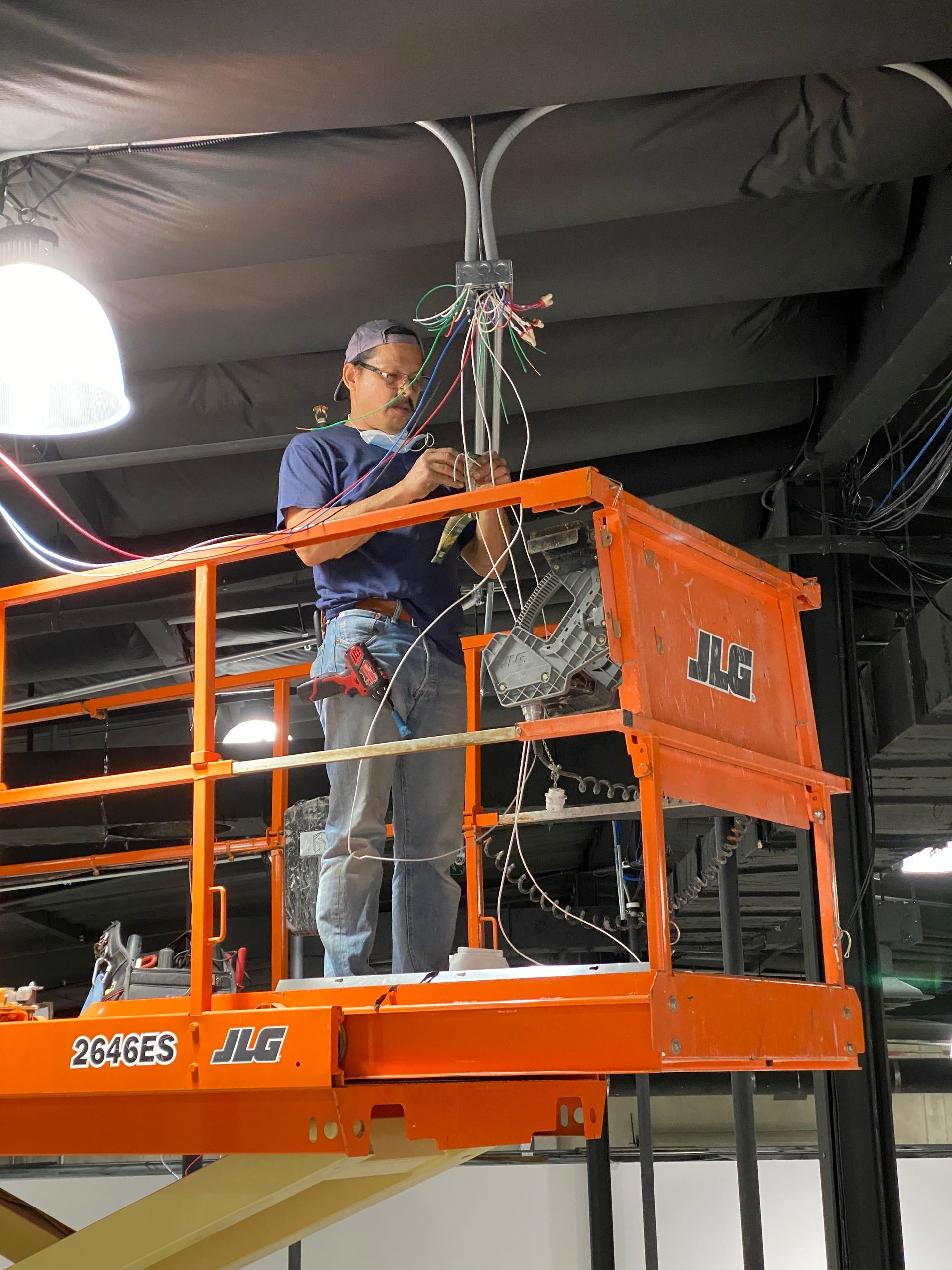 Worker on an orange lift platform installing cables overhead indoors