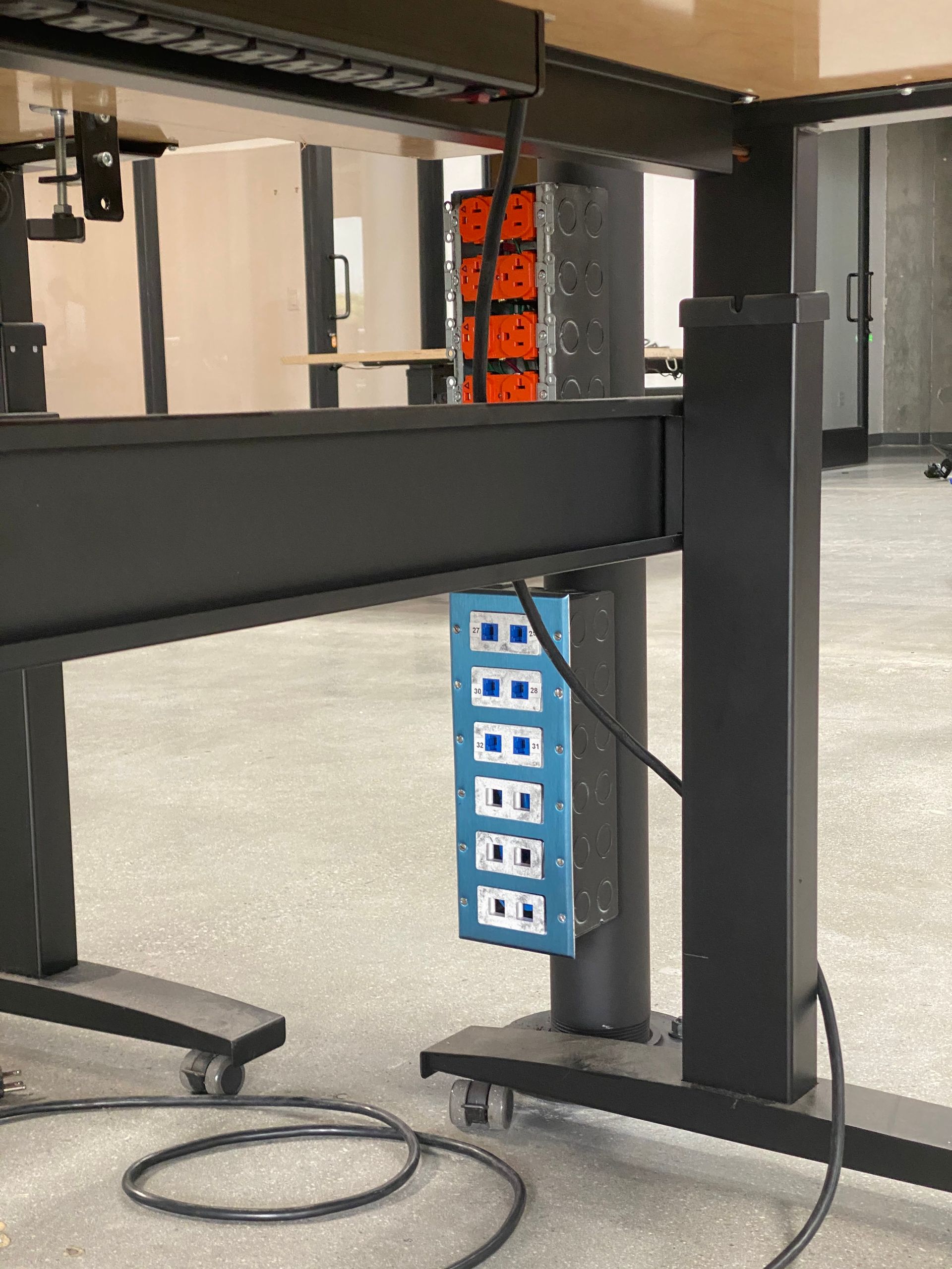 Adjustable desk frame with blue power strip and cords in an office setting
