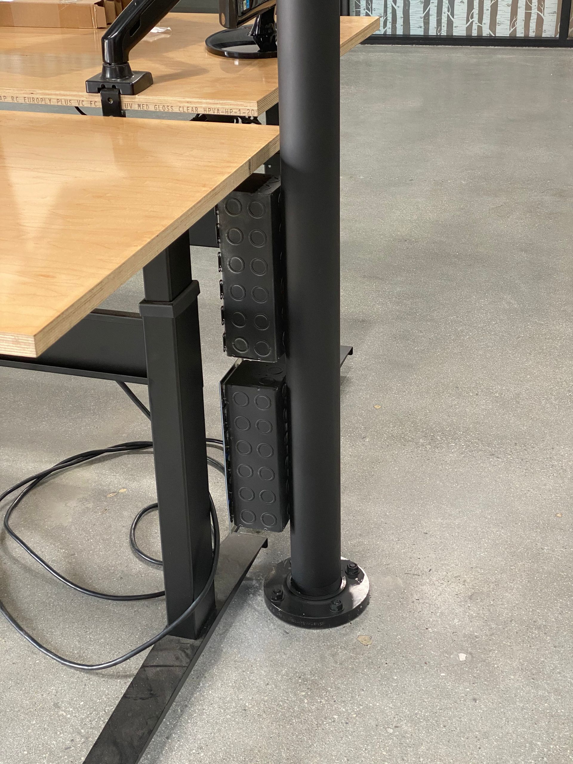 Black metal desk legs on a gray floor beside a light wood tabletop.