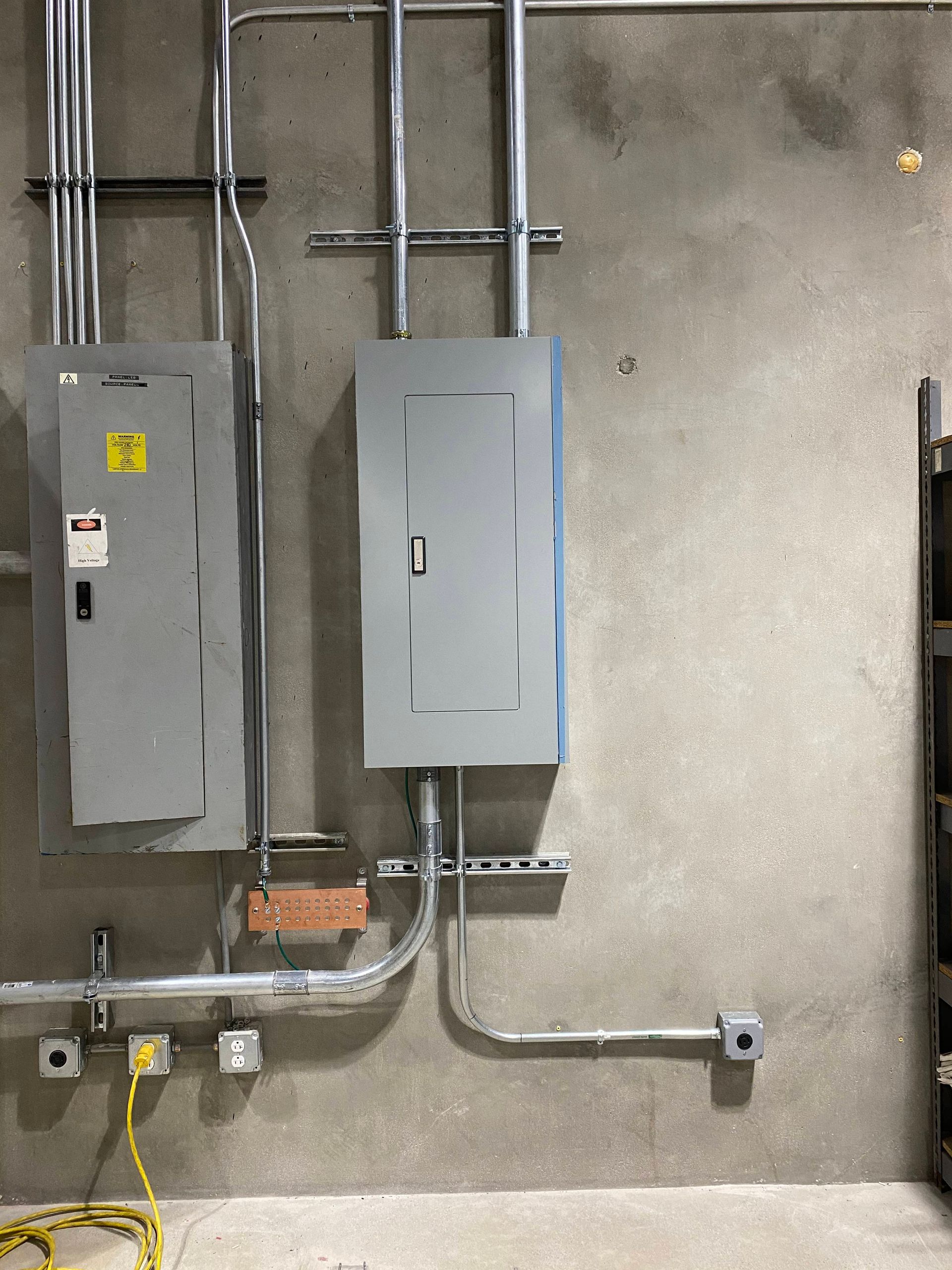 Two gray electrical panels on a concrete wall with conduit and wiring nearby