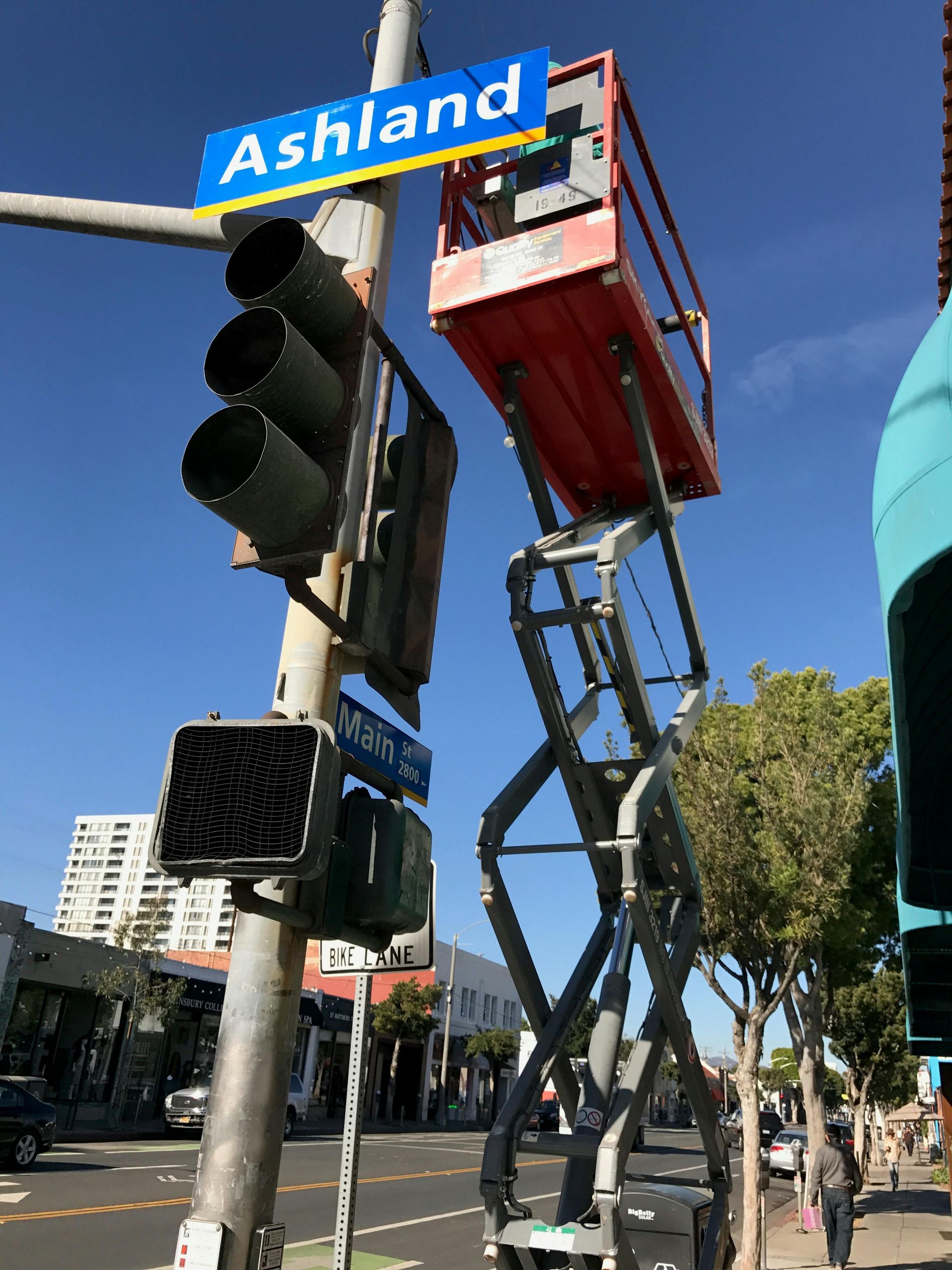A red scissor lift is extended next to a traffic light pole with an 