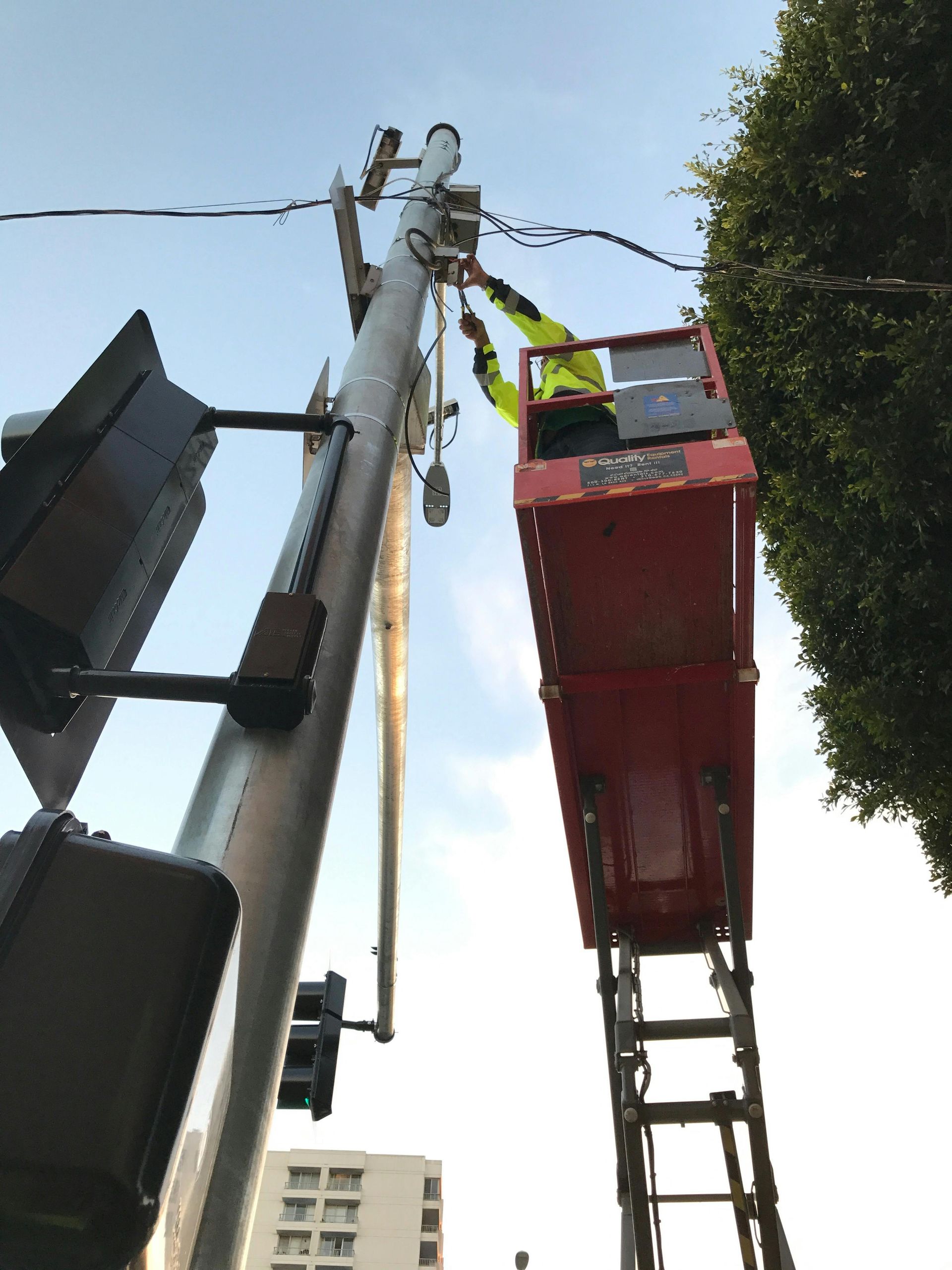 A technician in a high-visibility yellow shirt works from a red scissor lift on equipment atop a utility pole.