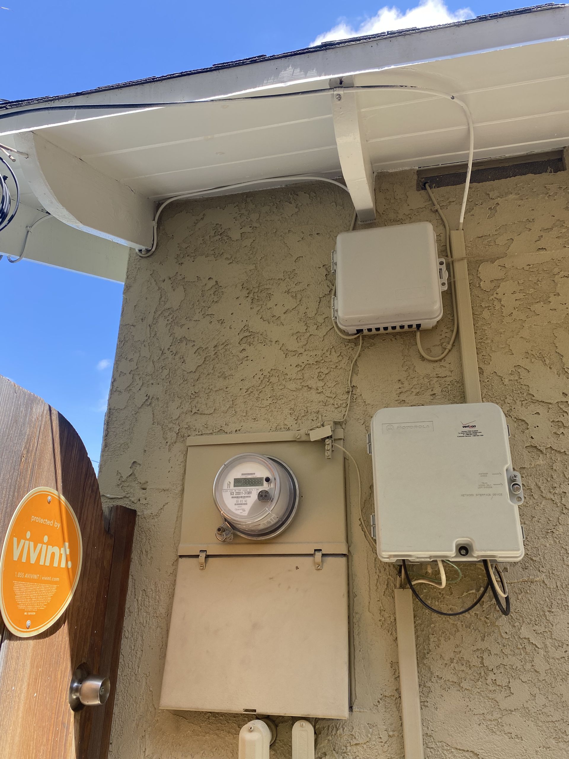 House exterior with a utility meter and electrical boxes mounted on a stucco wall under the eaves