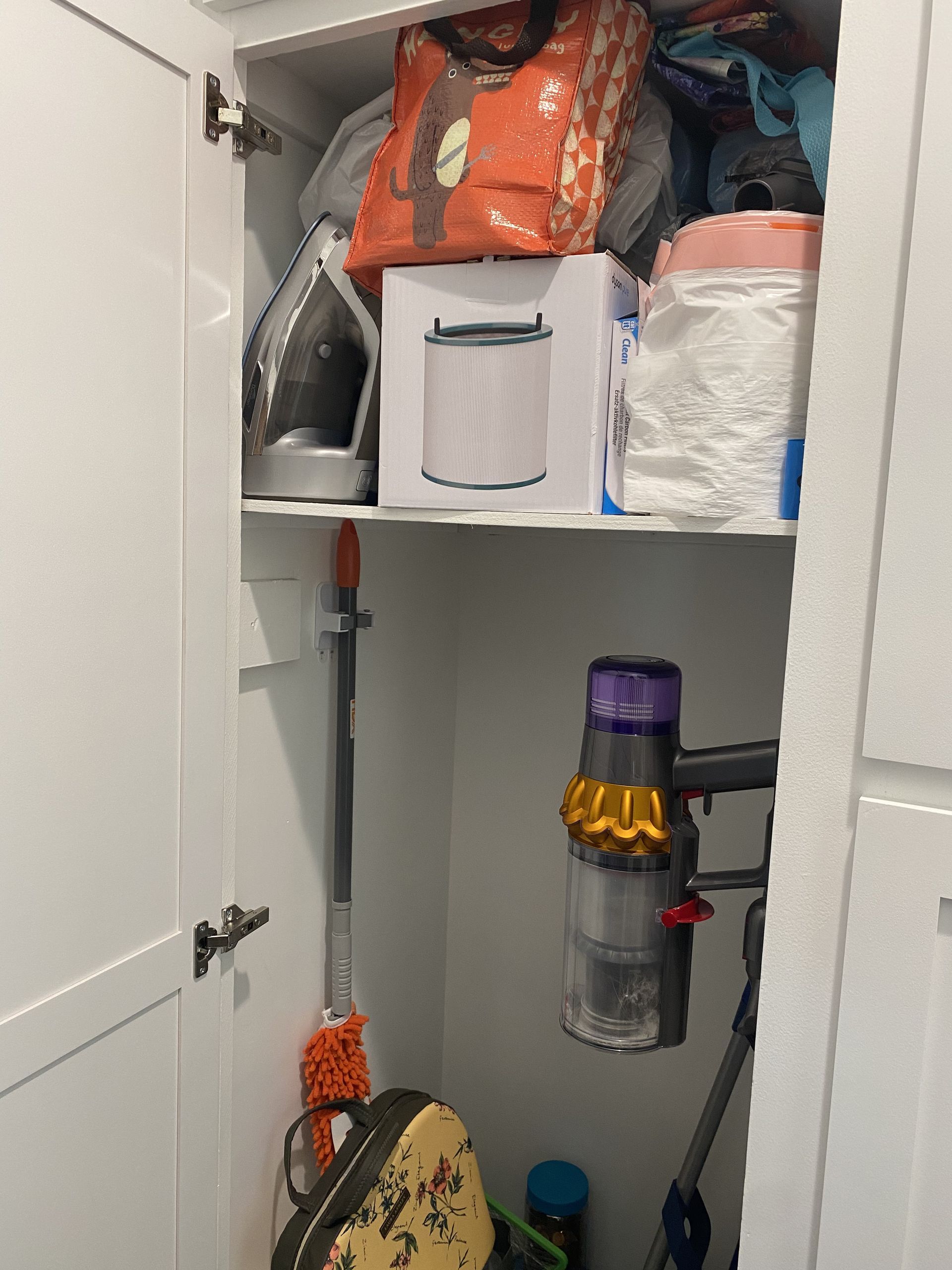 Open closet with shelves of storage bags, bins, and a hanging cordless vacuum cleaner.