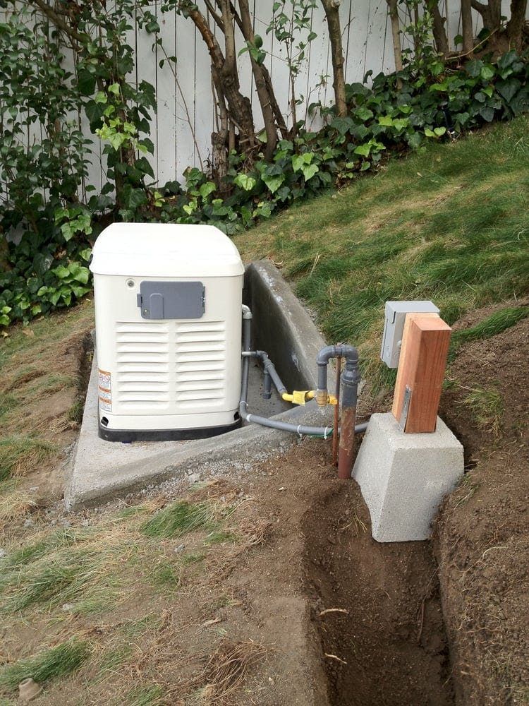 A white backup generator sits on a concrete pad in a yard next to an open trench, exposed electrical conduits, and a post.