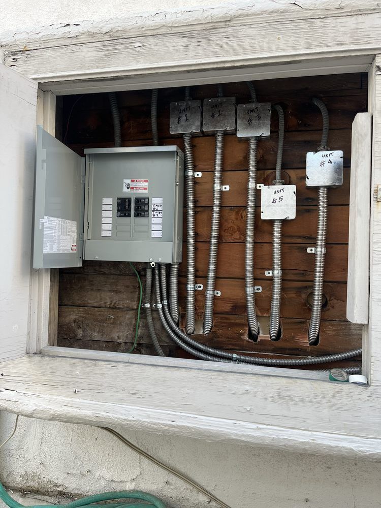 An electrical service panel and junction boxes mounted on an exposed wooden wall inside a recessed wall opening.