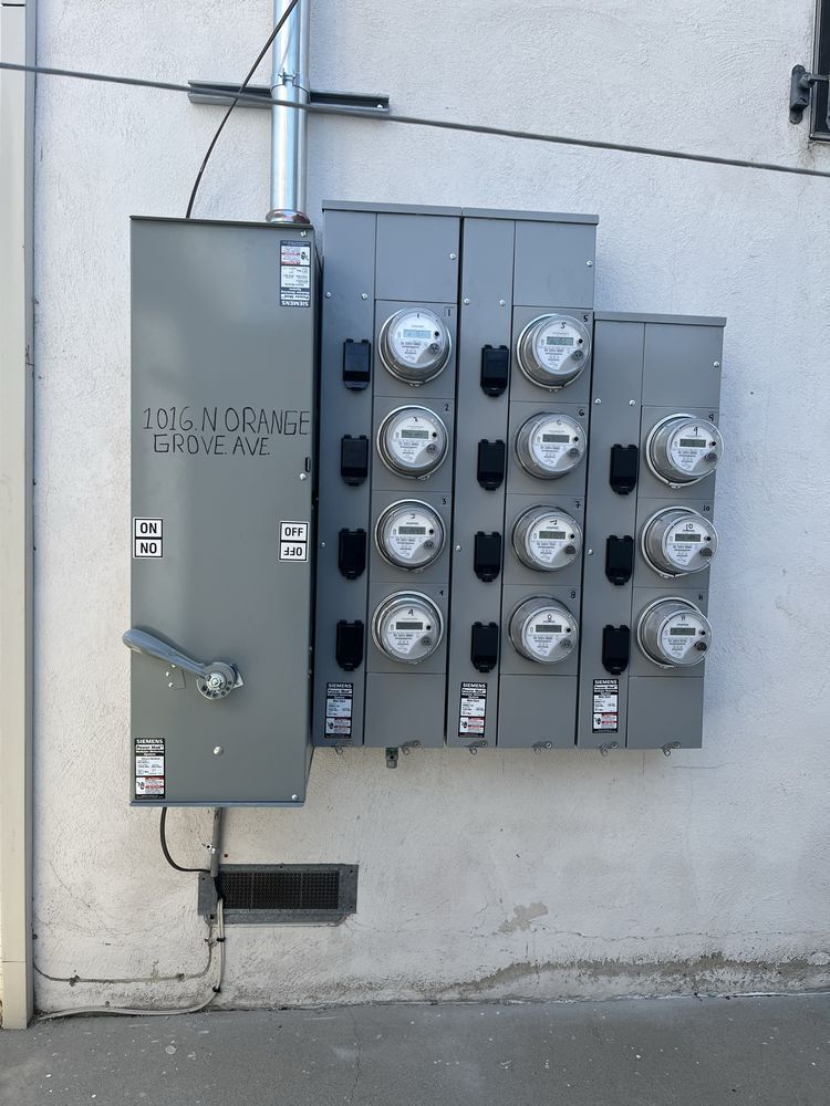 A gray electrical meter bank with a main disconnect switch mounted on a white exterior wall.