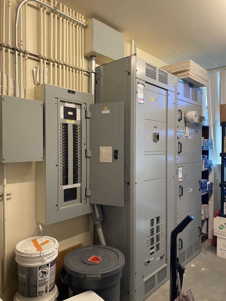 Electrical room featuring a gray breaker panel, large switchgear cabinet, and conduits mounted on the wall.