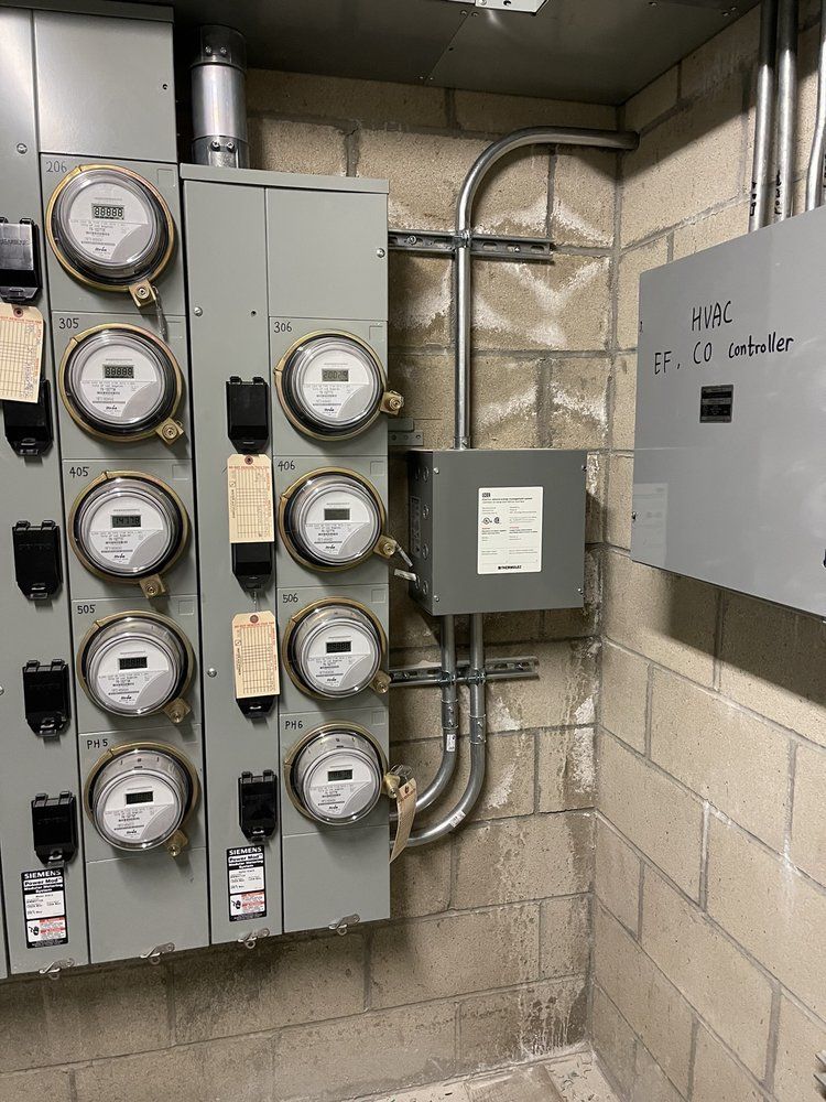 An electrical meter bank with conduit wiring and a junction box mounted on a concrete block wall.