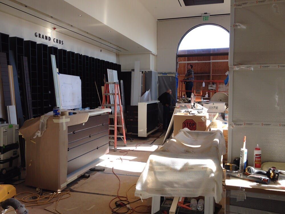 An interior space under renovation with furniture, tools, construction materials, and a ladder, lit by a large arched window.