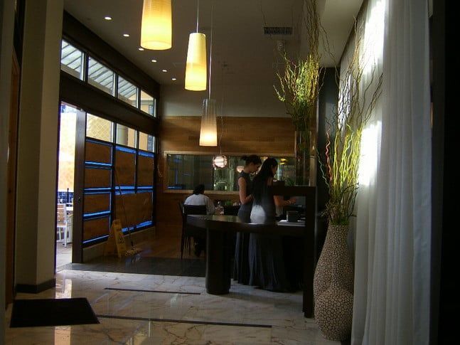 A hotel lobby interior with floor-to-ceiling windows, warm pendant lighting, wooden accents, and a reception desk.