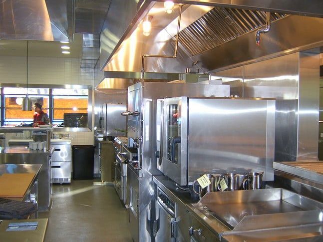 A professional kitchen with stainless steel equipment, a large oven, and a person working in the background.