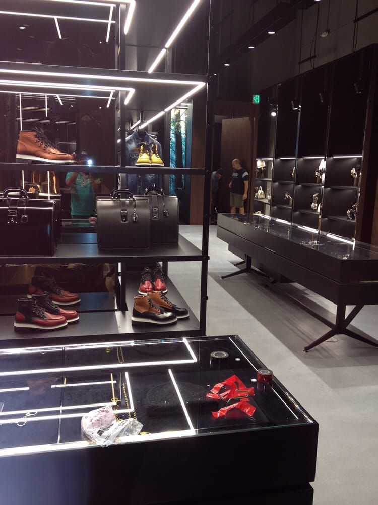 Retail display shelves with boots and bags under LED lighting in a modern store, with a person standing in the background.