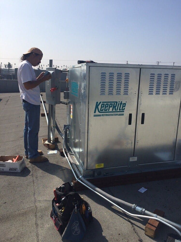 A technician works on the electrical disconnect of a KeepRite rooftop HVAC unit on a sunny day.