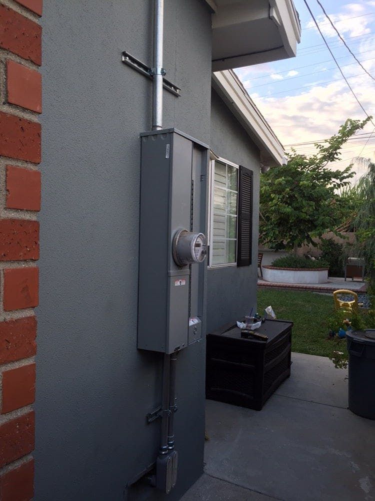 An electrical meter installed on the gray exterior wall of a house, with a conduit running vertically above it.