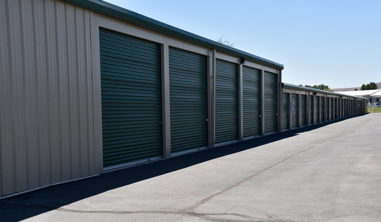 A row of storage units with green doors on a sunny day.