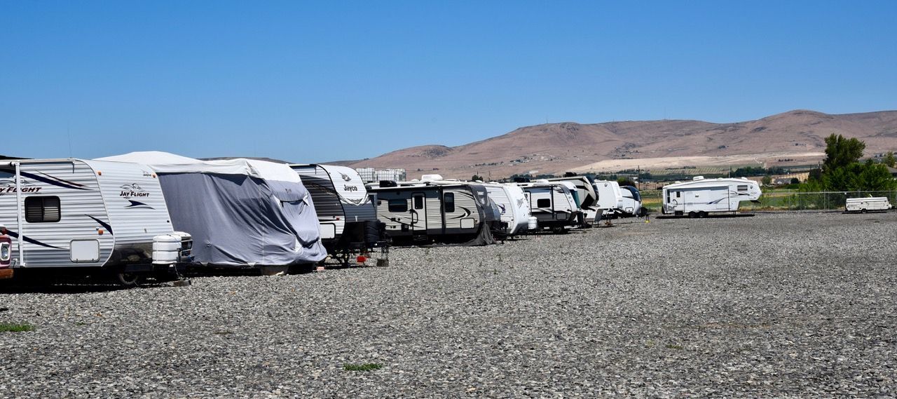 A row of rvs parked in a gravel lot with mountains in the background.