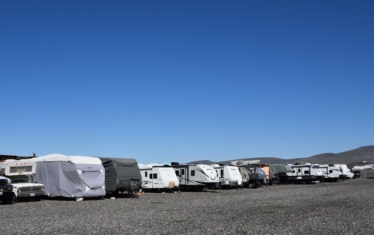 A row of rvs are parked in a gravel lot.