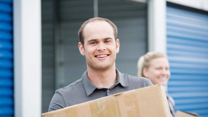 A man is holding a cardboard box in front of a storage unit.