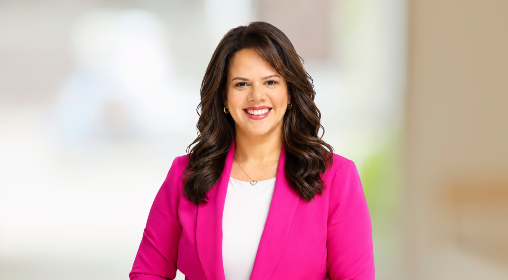Julissa Henriquez, smiling woman in a bright pink blazer against a softly blurred background