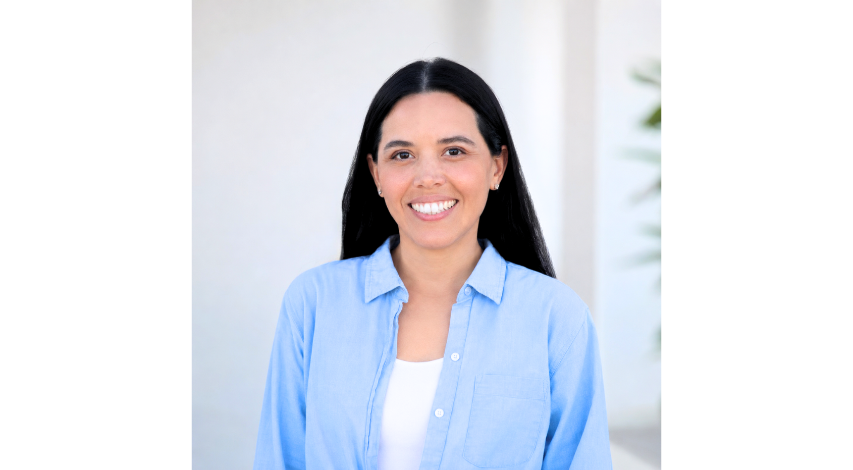 Lesly Harden, smiling woman in a light blue shirt standing against a bright white background