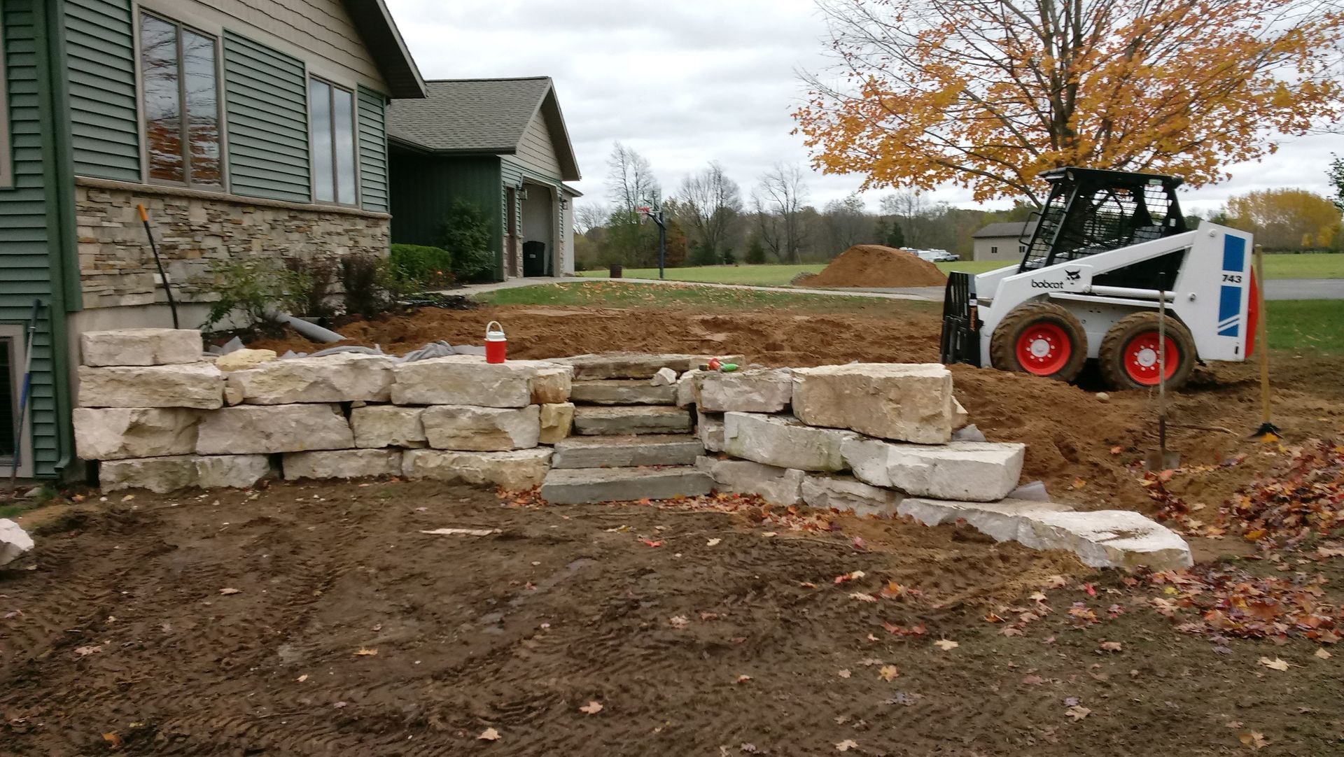 A bobcat is working on a stone wall in front of a house.