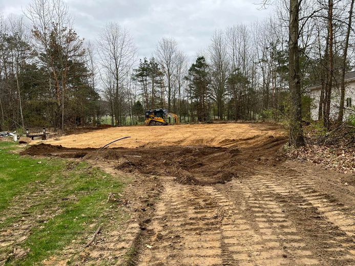 A bulldozer is moving dirt in a field surrounded by trees.