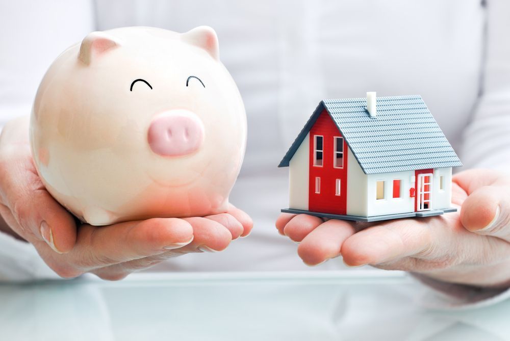 A Person is Holding a Piggy Bank and a Model House in Their Hands — Richardson Conveyancing in Hunter Valley, NSW