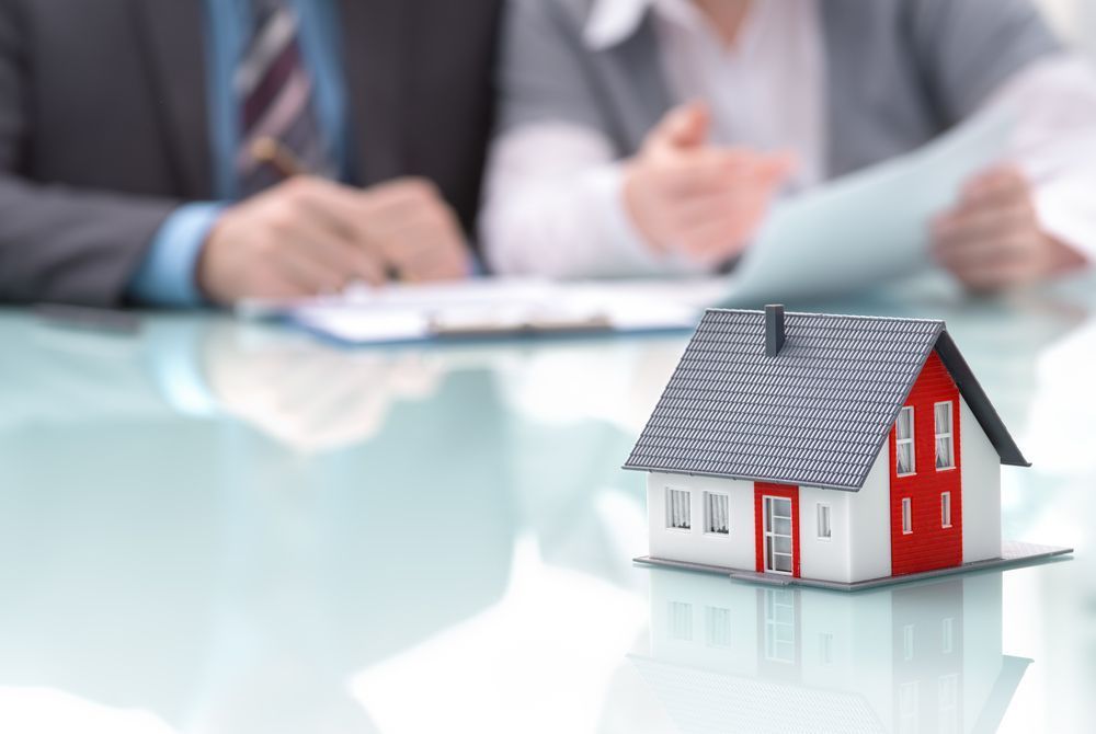 A Couple is Sitting at a Table With a Model House on It — Richardson Conveyancing in Wollongong, NSW