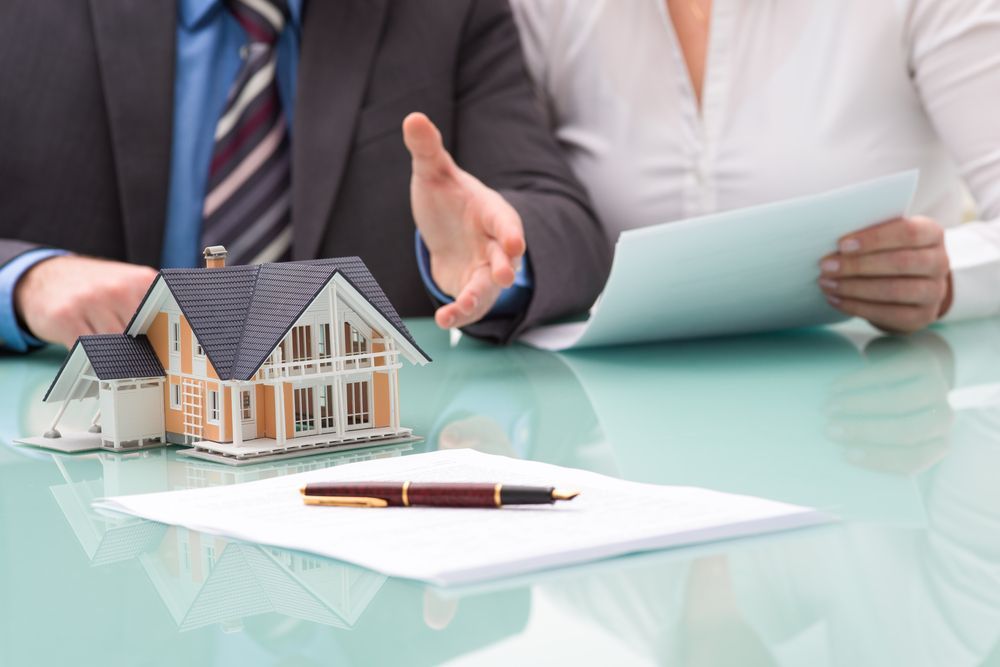 A Man and a Woman Are Sitting at a Table With a Model House on It — Richardson Conveyancing in Mudgee, NSW