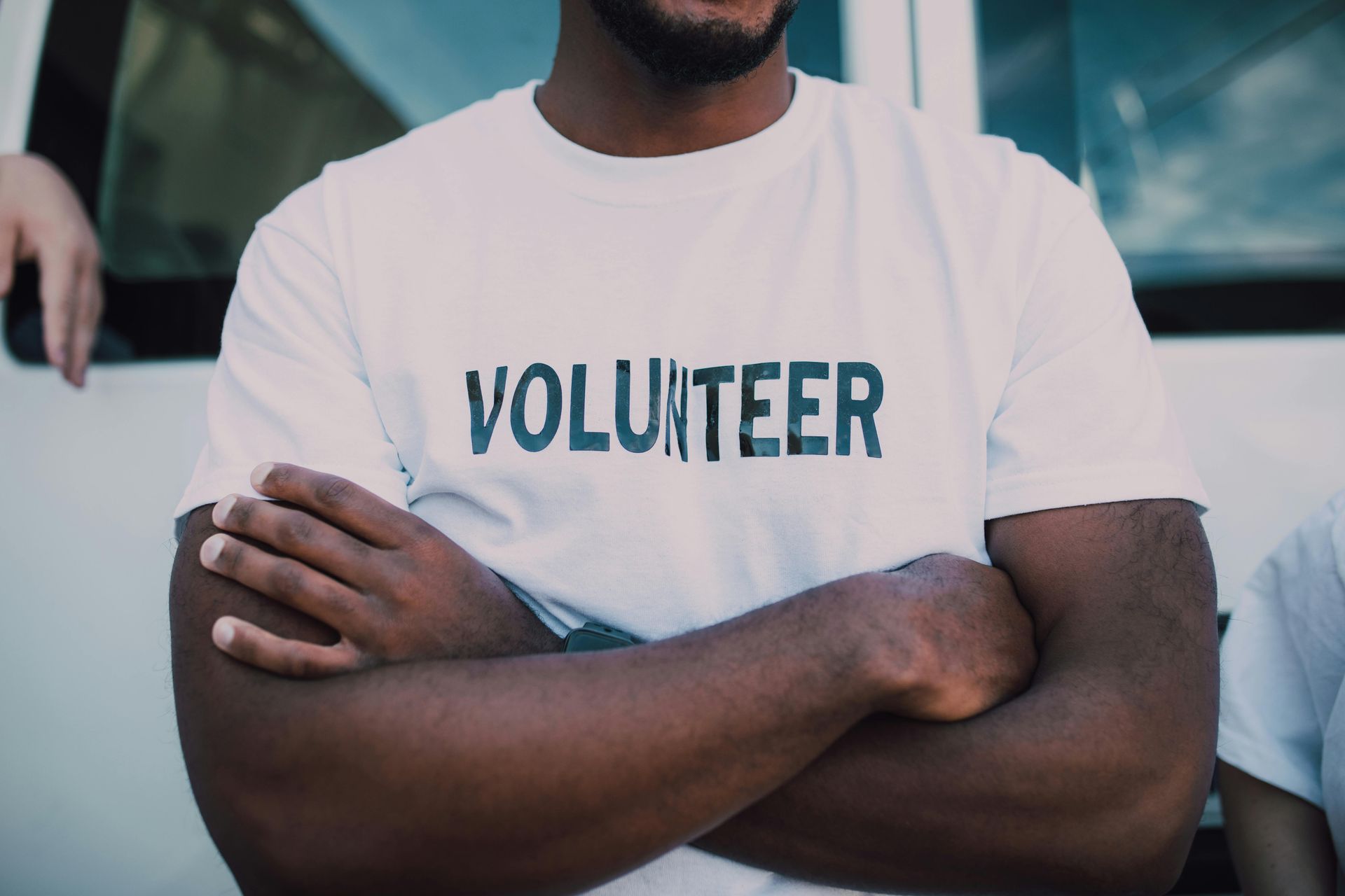 A man wearing a white volunteer t-shirt with his arms crossed. - abraham sanieoff
