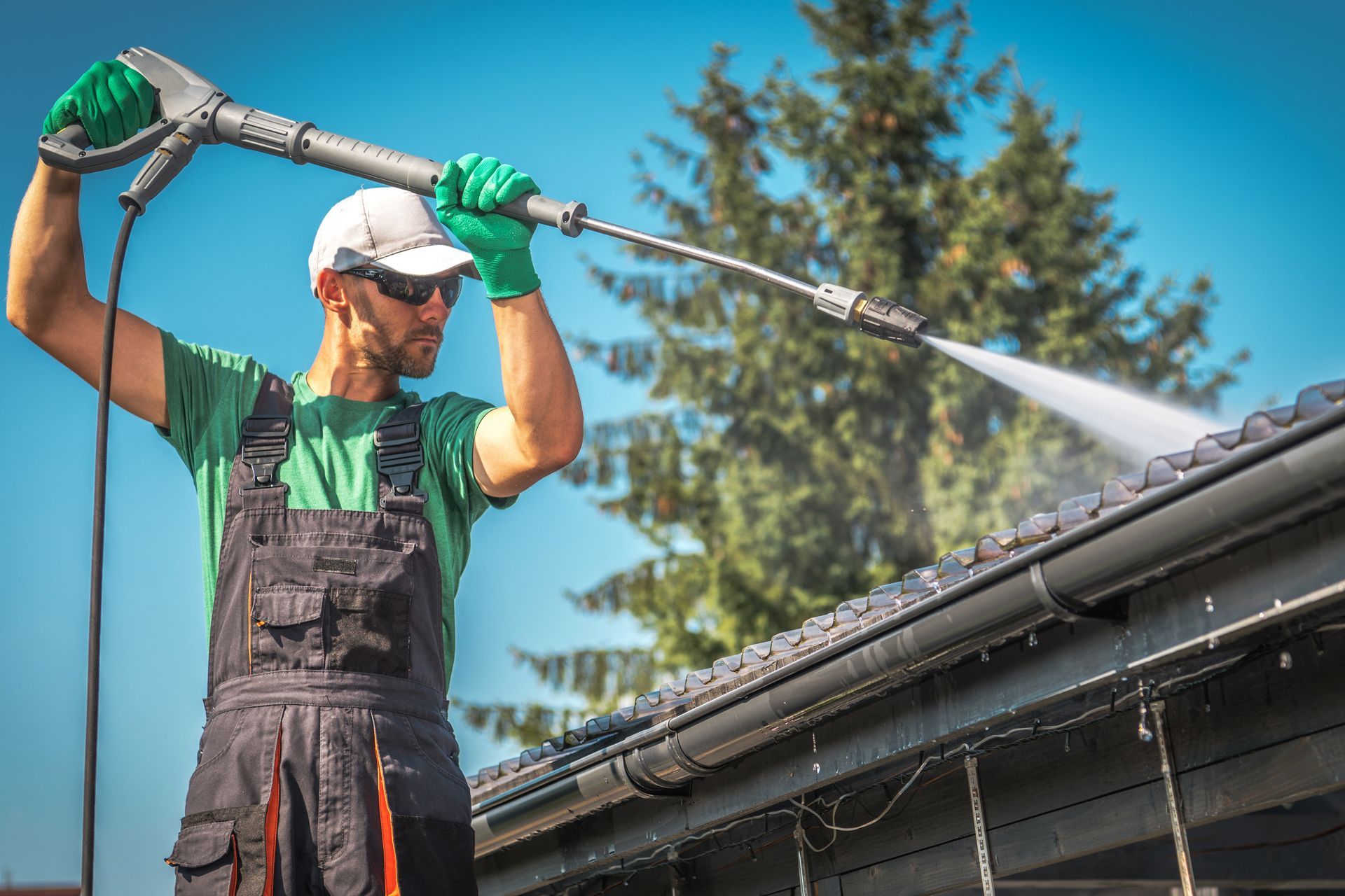 Worker in green gloves pressure washing a roof on a sunny day