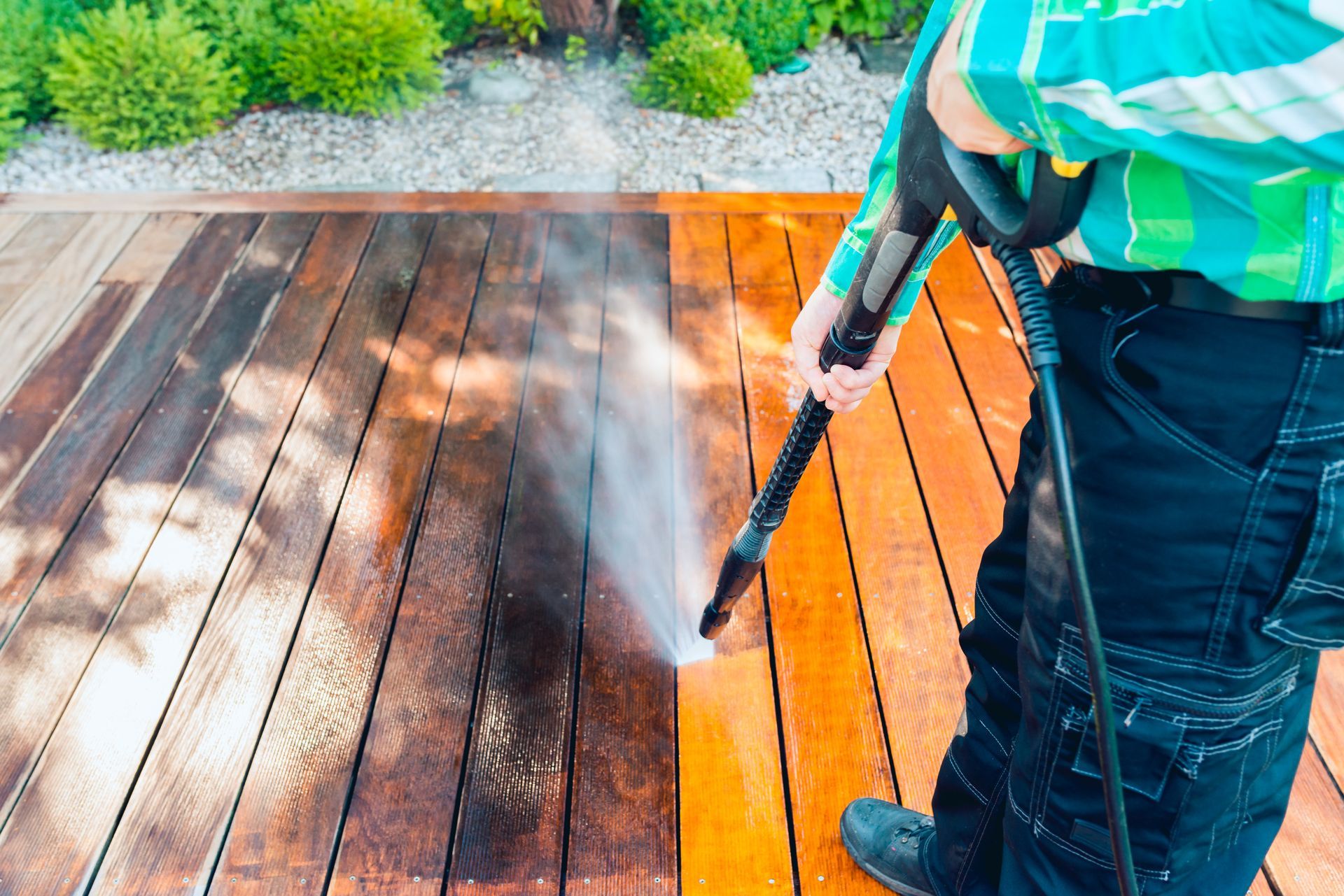 Person pressure-washing a wooden deck with orange and dark stained boards.