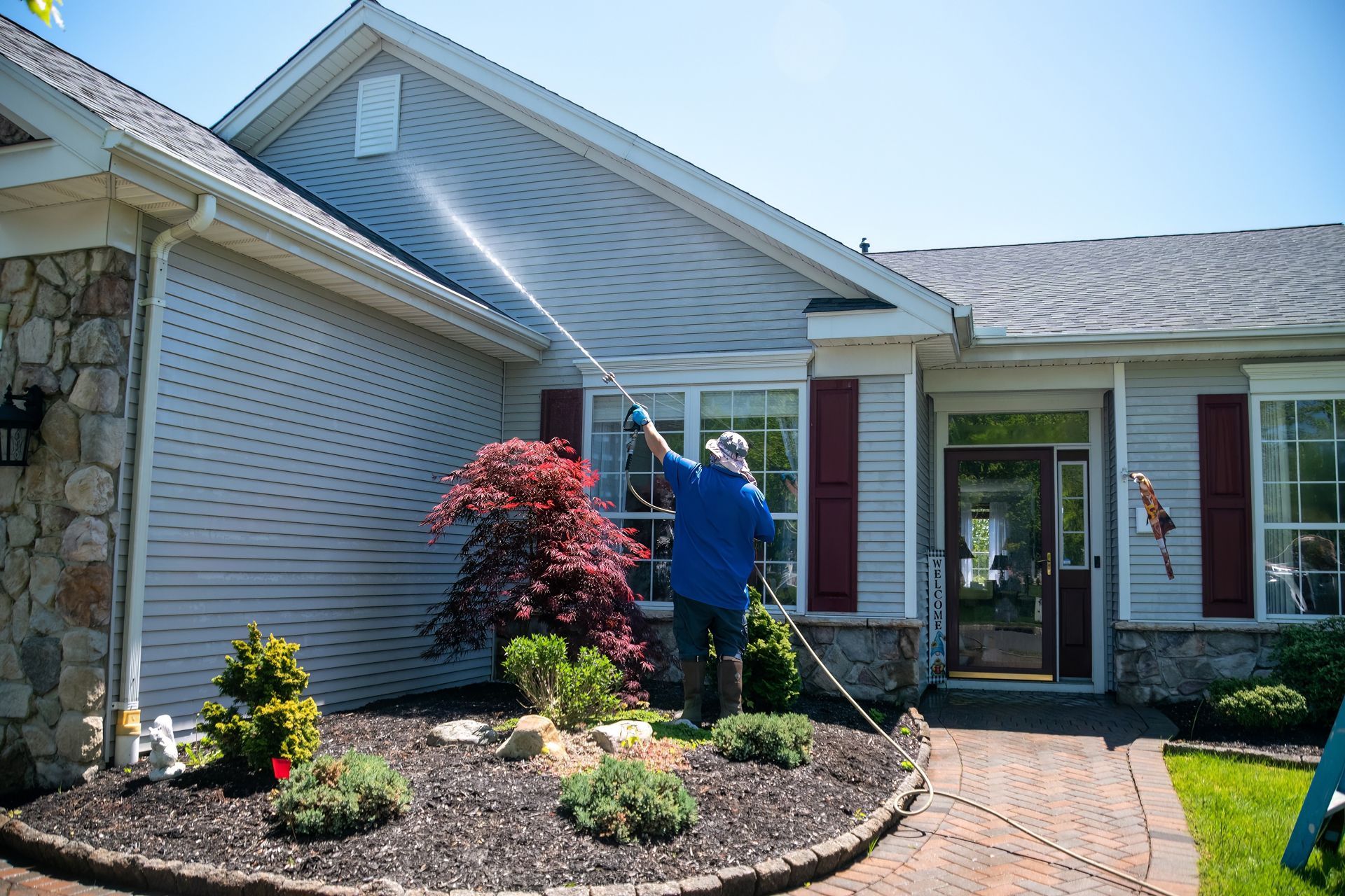 Person cleaning gutters on a suburban house exterior with a ladder and blue shirt