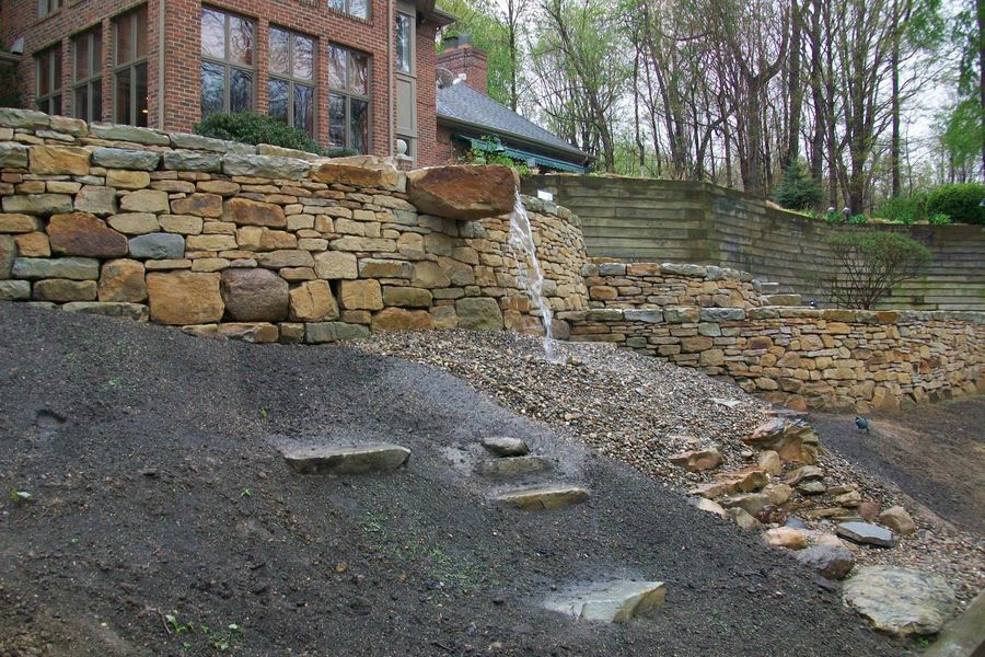 A stone wall with a waterfall in front of a house