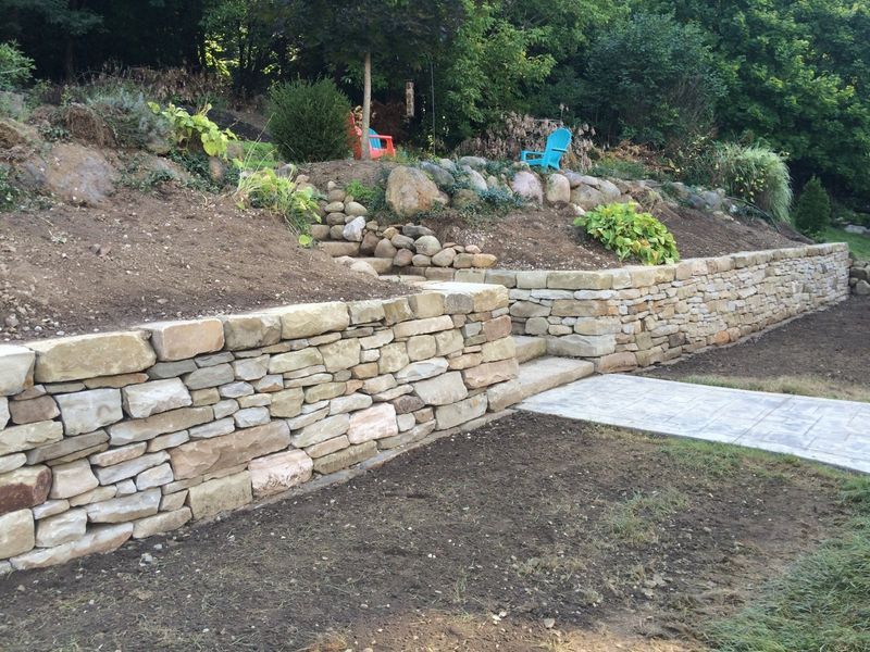 A stone wall surrounds a lush green hillside in a backyard.